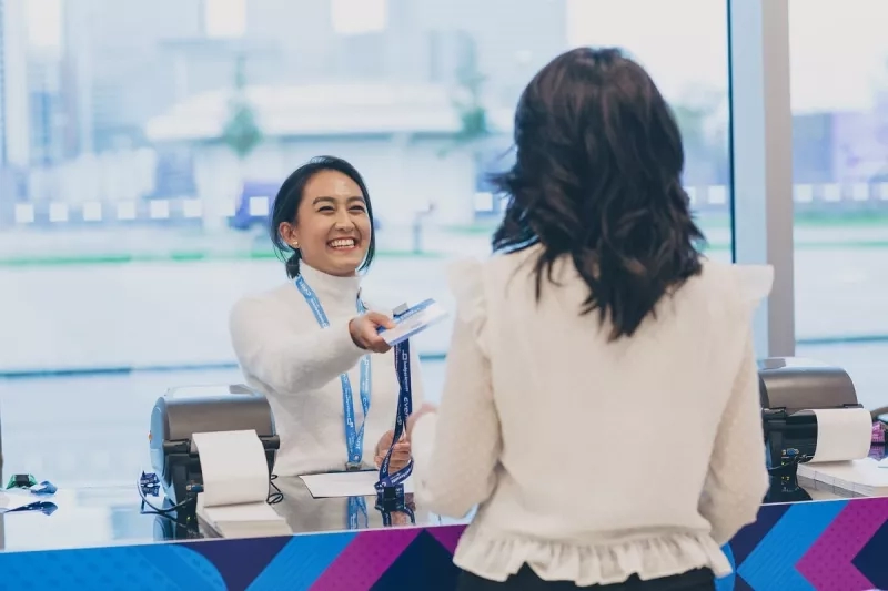 A smiling receptionist handing over an event management software badge to a participant at a green event.