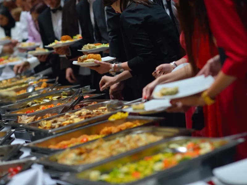 A group of people are picking up food from a buffet table, which is filled with different dishes.