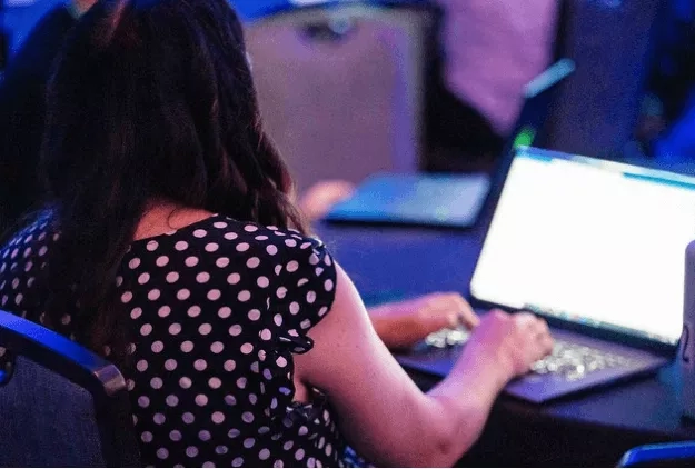 A woman sitting at a table using a laptop at an event with event reminder email tips.