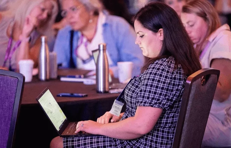 A woman sitting at a table with a laptop working on event reminders for a conference.