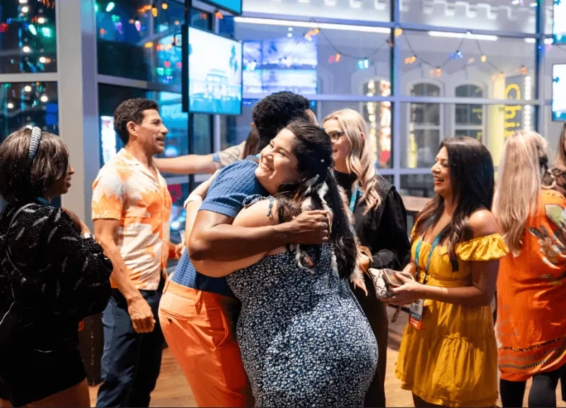 People engaging in interactive event ideas like hugging and socializing in a lively, colorful indoor setting.