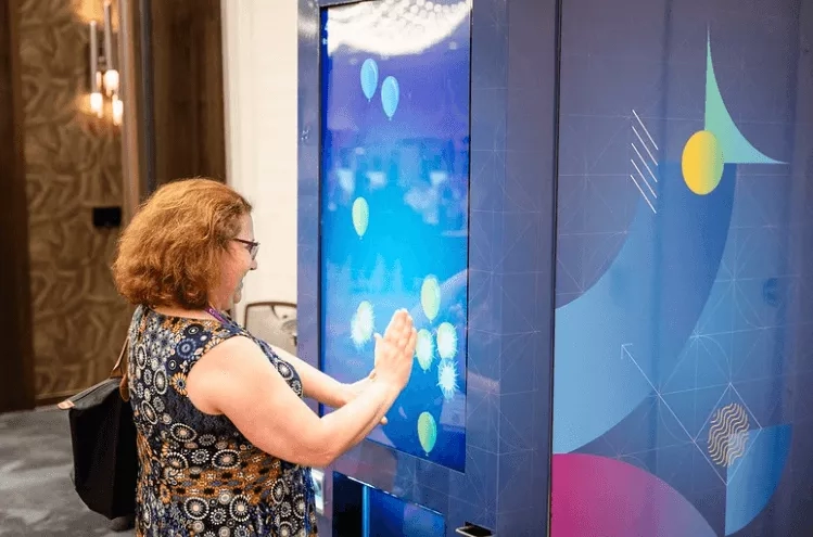 A woman is playing a game on a large interactive screen with a blue background.