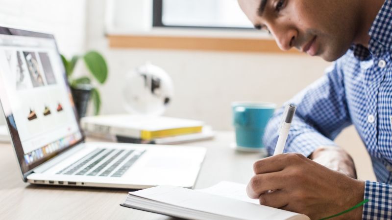 man taking notes while using laptop