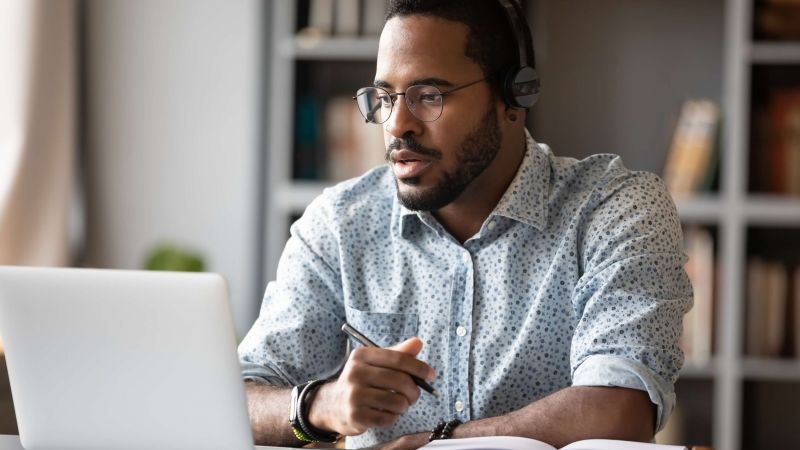 man taking notes while on laptop with headset