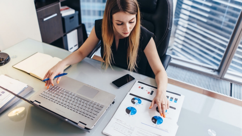 businesswoman looking at diagrams on computer and paper