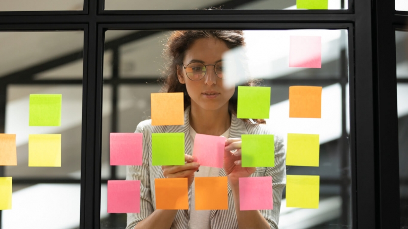 woman brainstorming ideas with post-it notes on glass