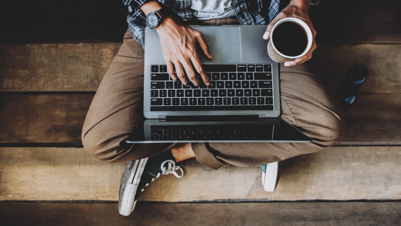 man holding coffee and working on email marketing campaign on laptop