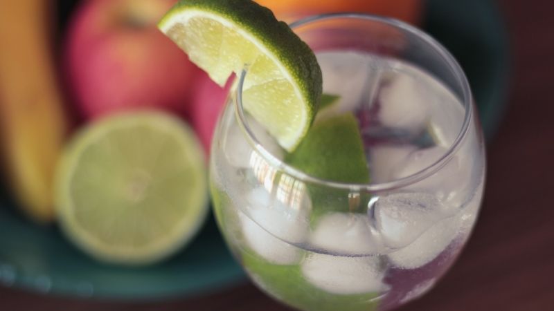 clear drink in glass with ice and lime