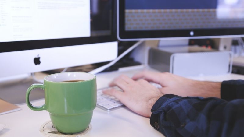 Person typing on desktop with coffee on desk