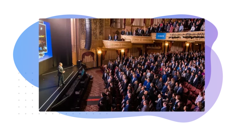 A man is standing on stage in front of a large crowd in an auditorium.